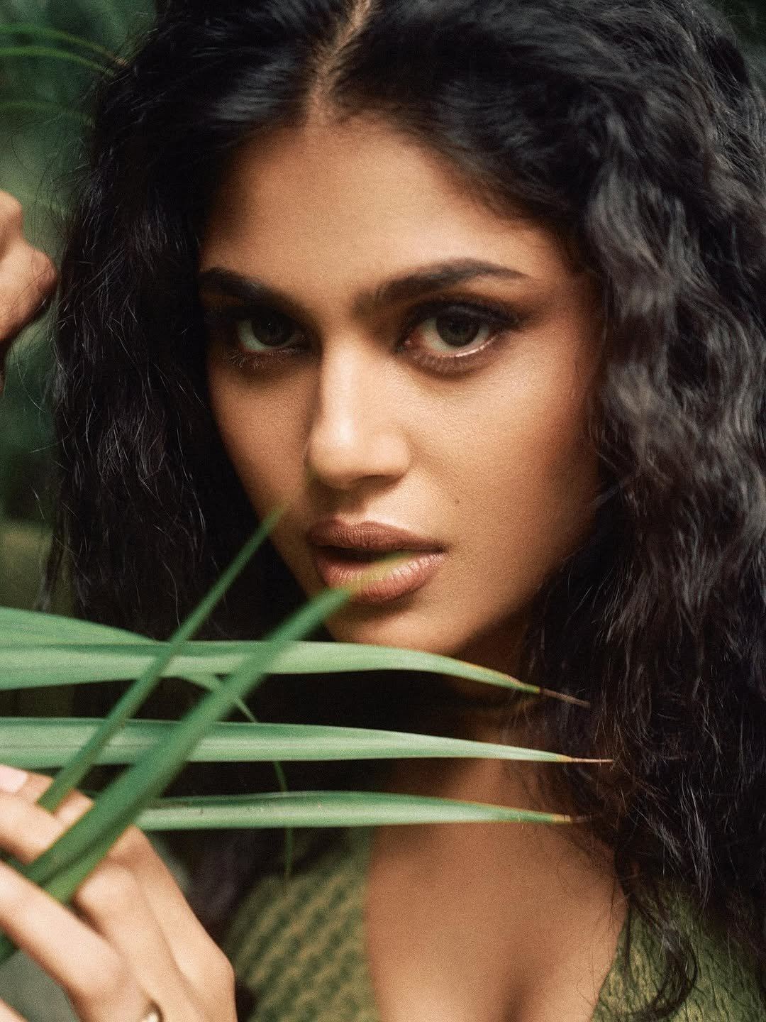 The actress looks alluring in a green outfit surrounded by foliage.