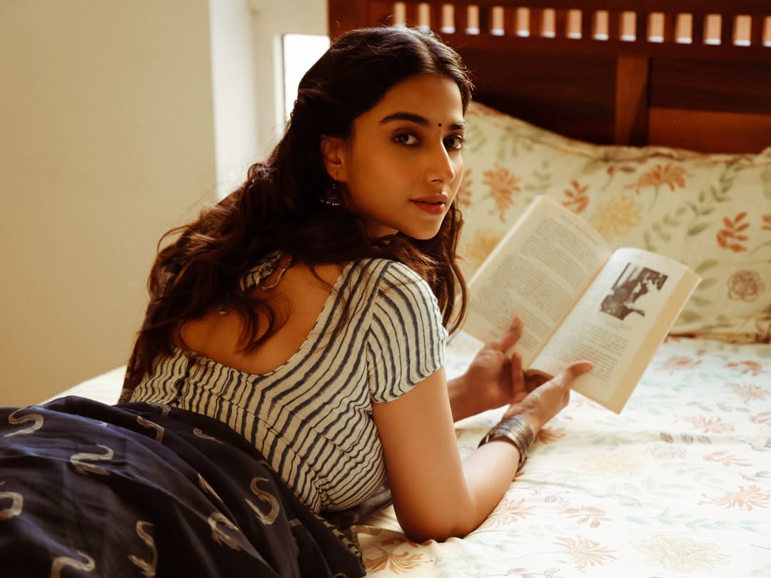 Meenakshi Chaudhary Posing With Book On Bed