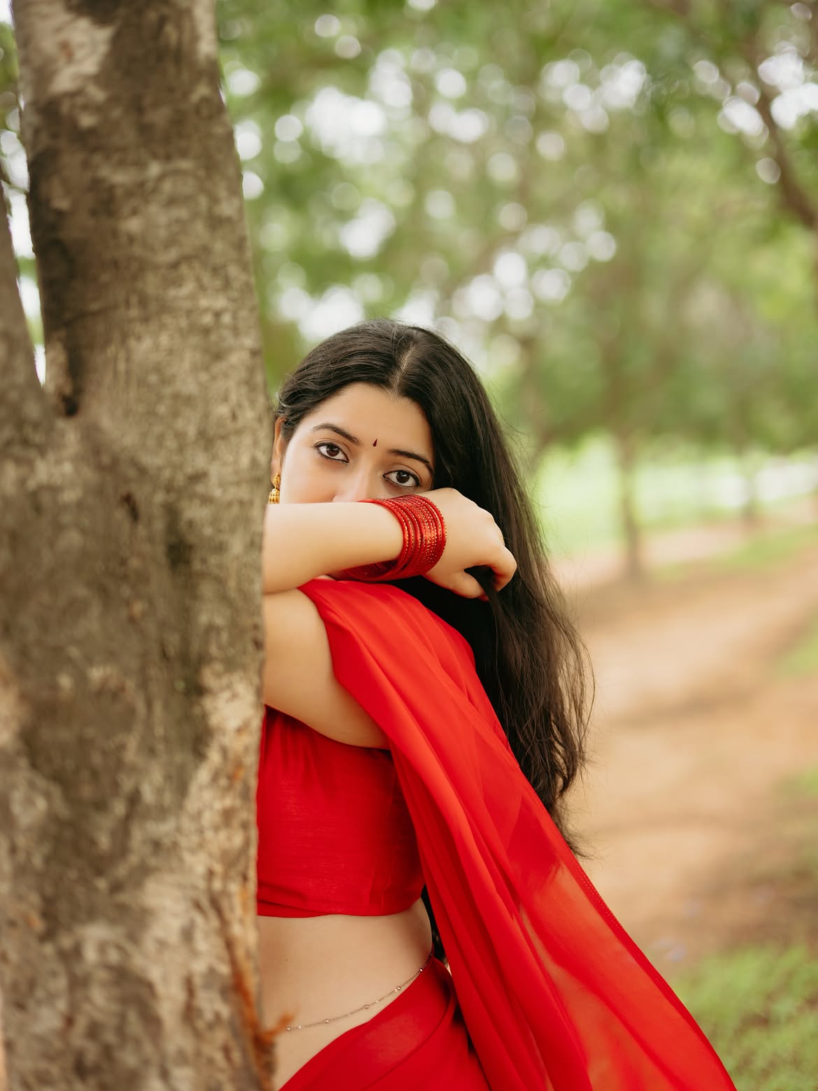 K Sudha Peeking Playfully From Behind Tree Trunk