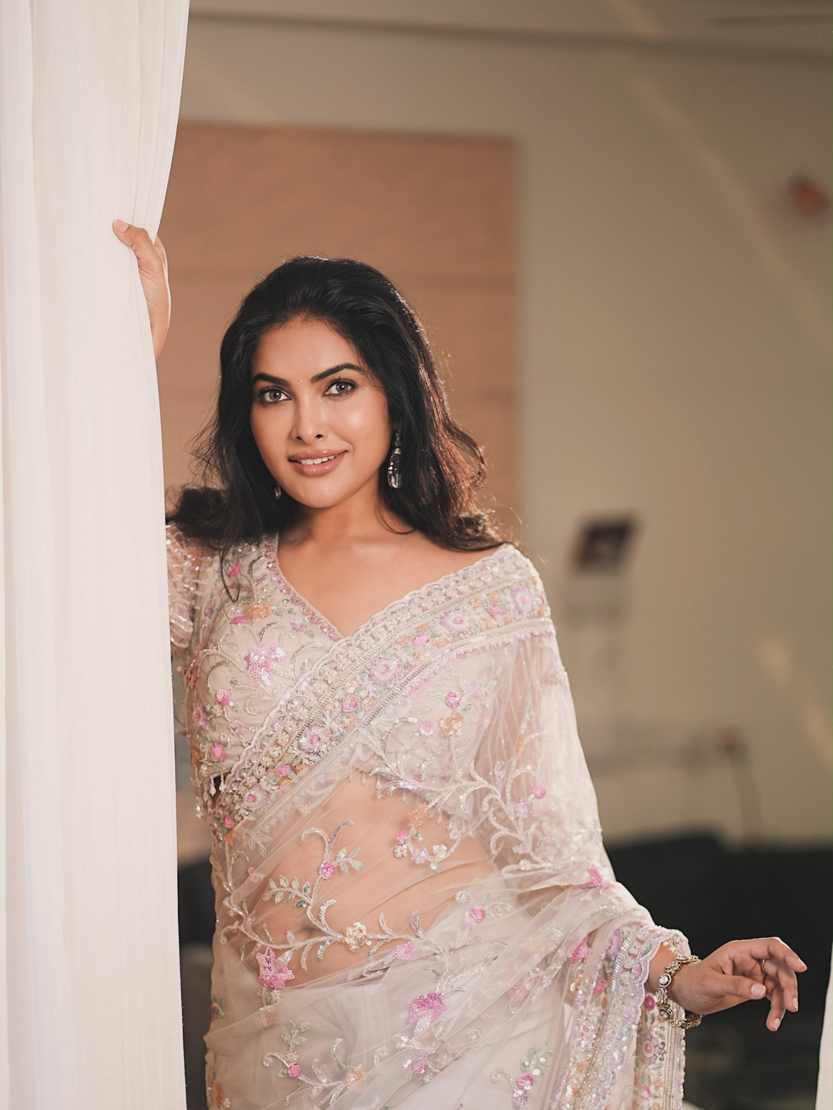 Divi Vadthya Poses Beside A White Curtain Panel!