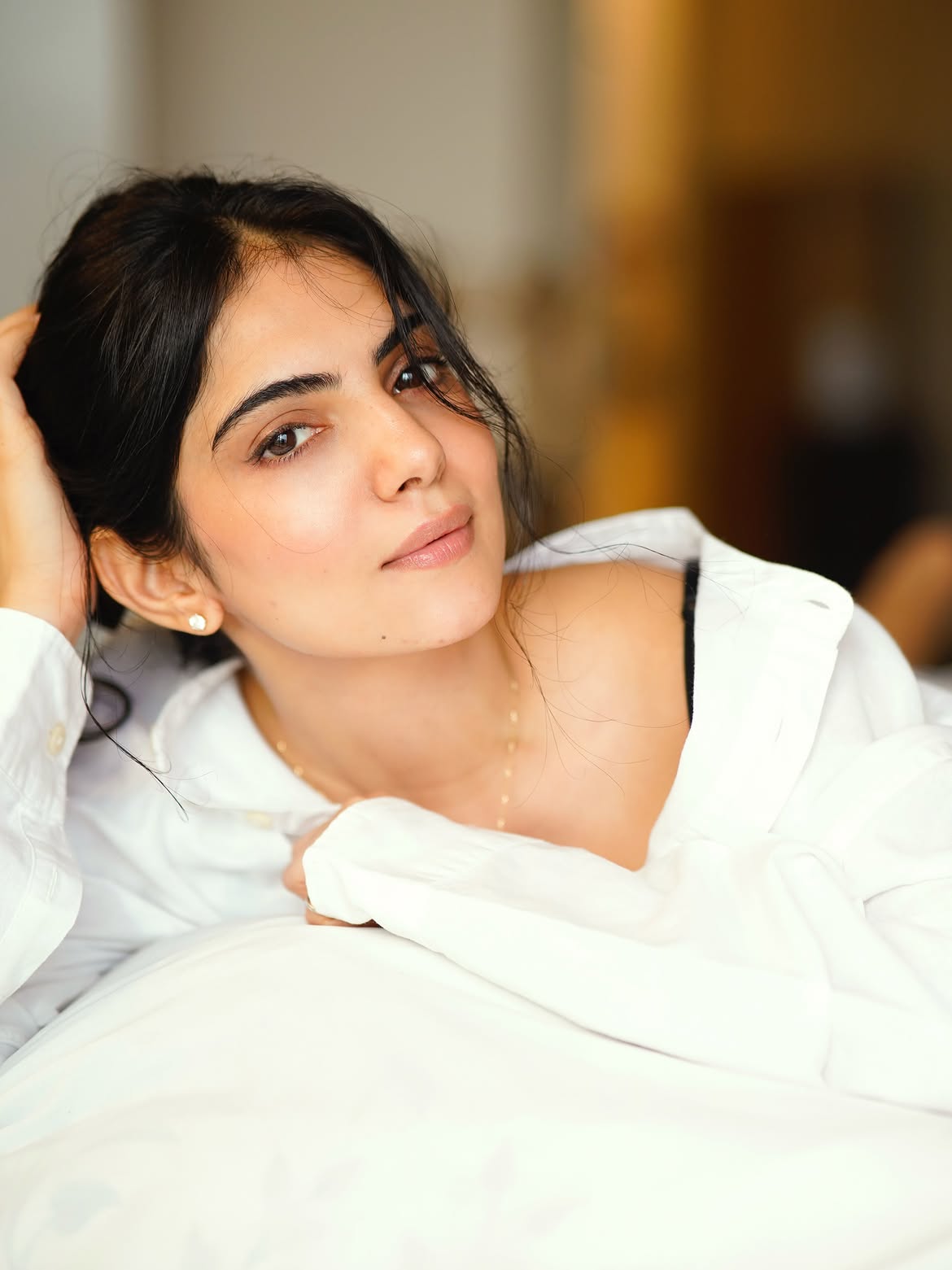 Misha Narang Rests On A Bed In A White Shirt Look
